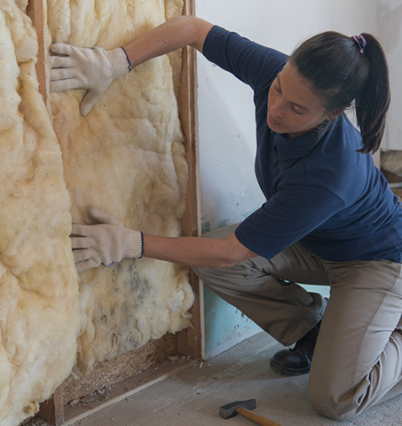 A woman installs insulation over a wall at a house.