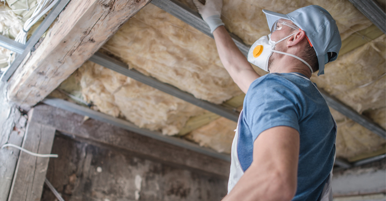 A man is wearing a mask while installing insulation.