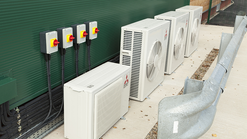 Several variable refrigerated flow units on the ground in front of commercial building. 