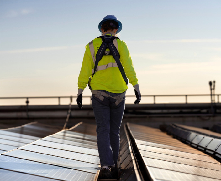 A worker walks on a roof lined with solar panels during sunset.