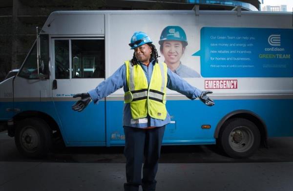 Un empleado de Con Edison de pie cerca de un camión de trabajo, con los brazos abiertos y una sonrisa.
