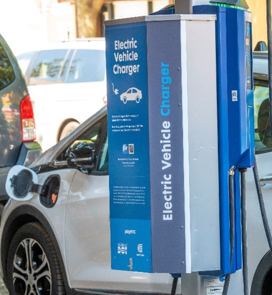 An electric vehicle charging station in front of a white electric car.