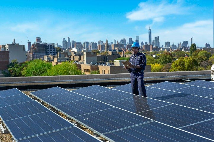 A Con Edison employee is standing on a building's roof that has solar panels installed on it.