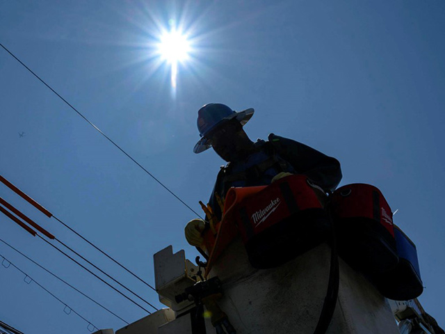 Un empleado de Con Edison trabaja en cables aéreos desde un camión grúa en un día soleado.