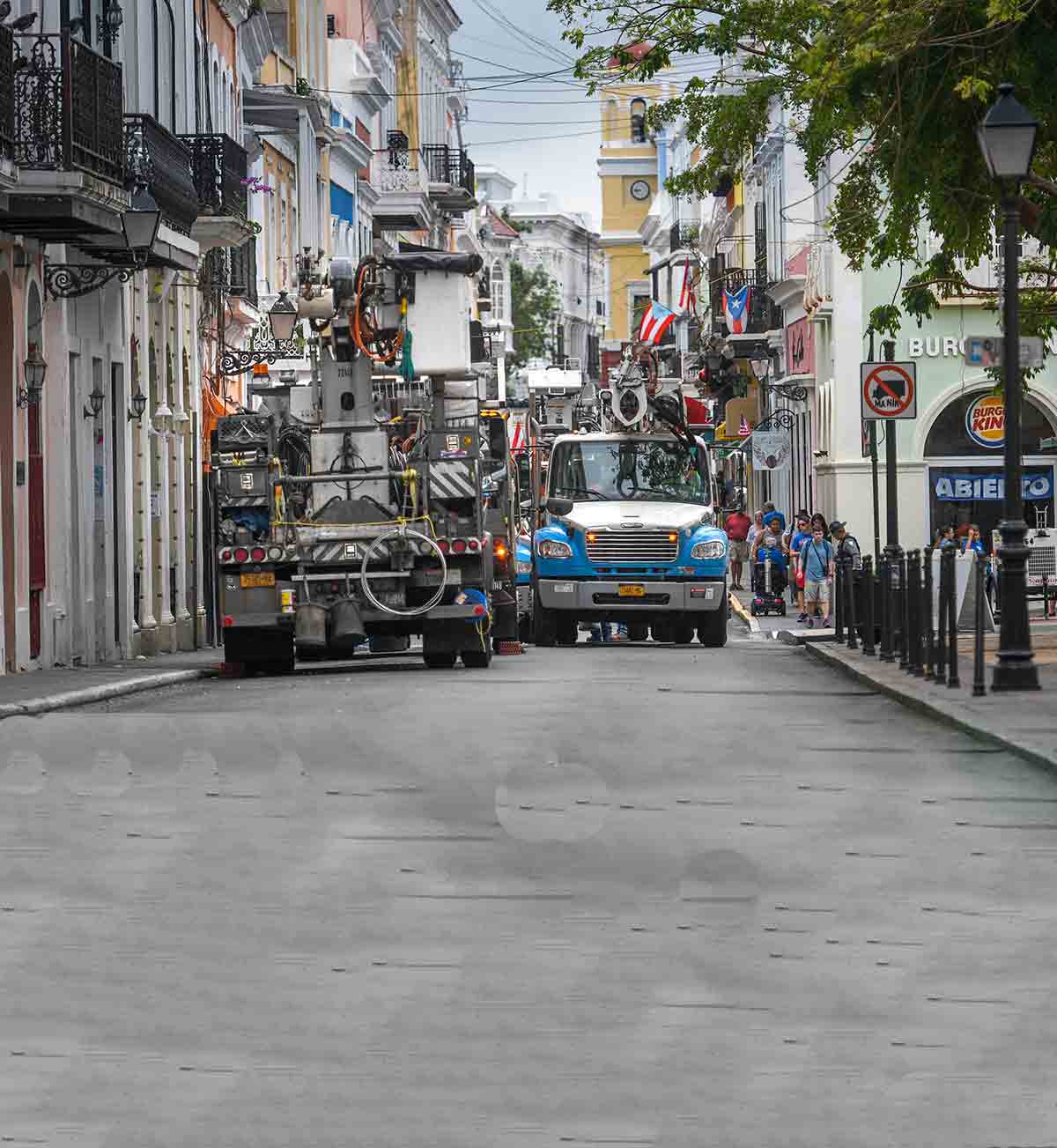Camiones grúa de Con Edison estacionados en una calle estrecha de un barrio de Puerto Rico.