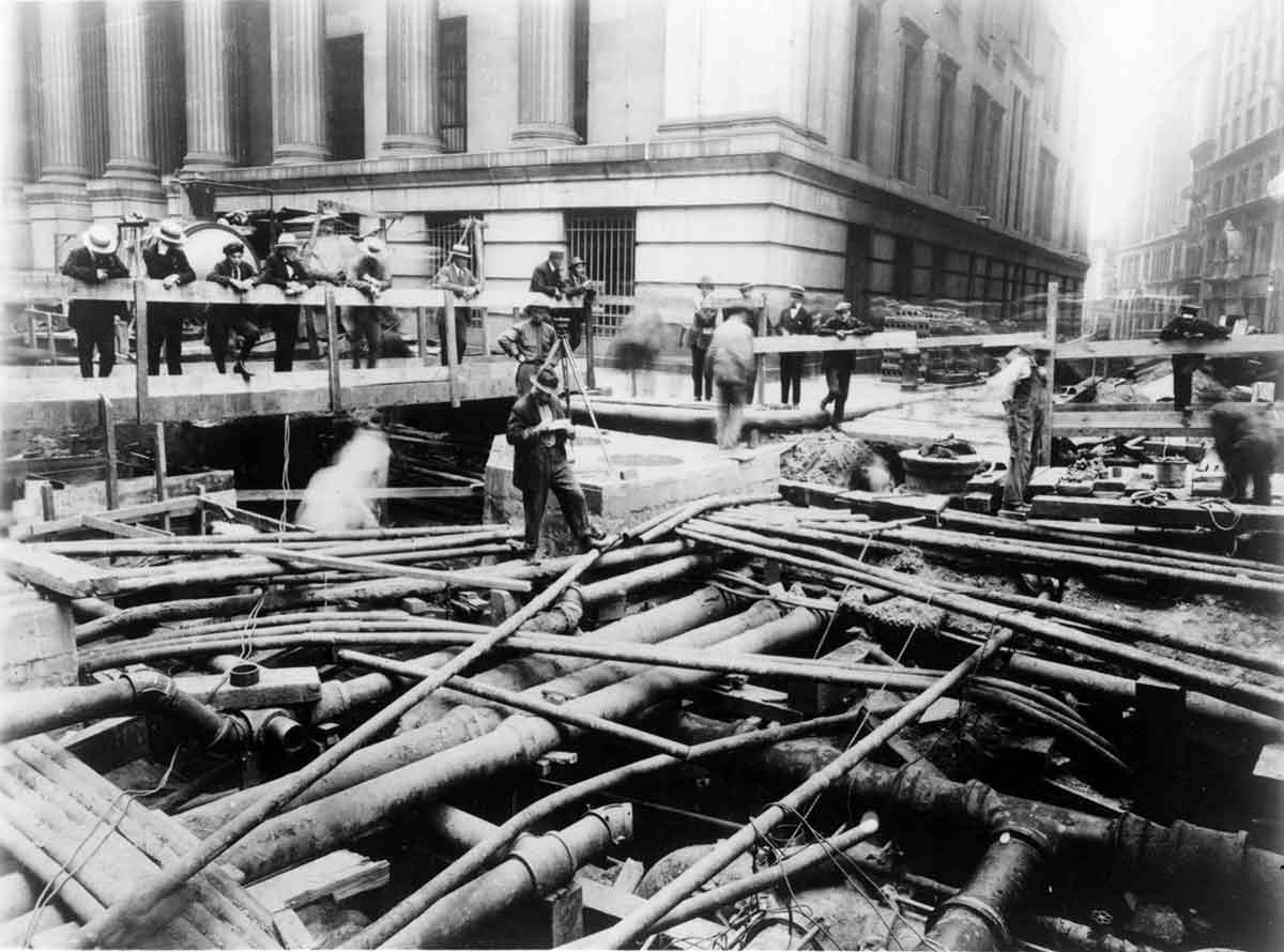 Fotografía histórica de una obra de la ciudad de Nueva York que muestra una gran cantidad de tuberías y personas mirando.
