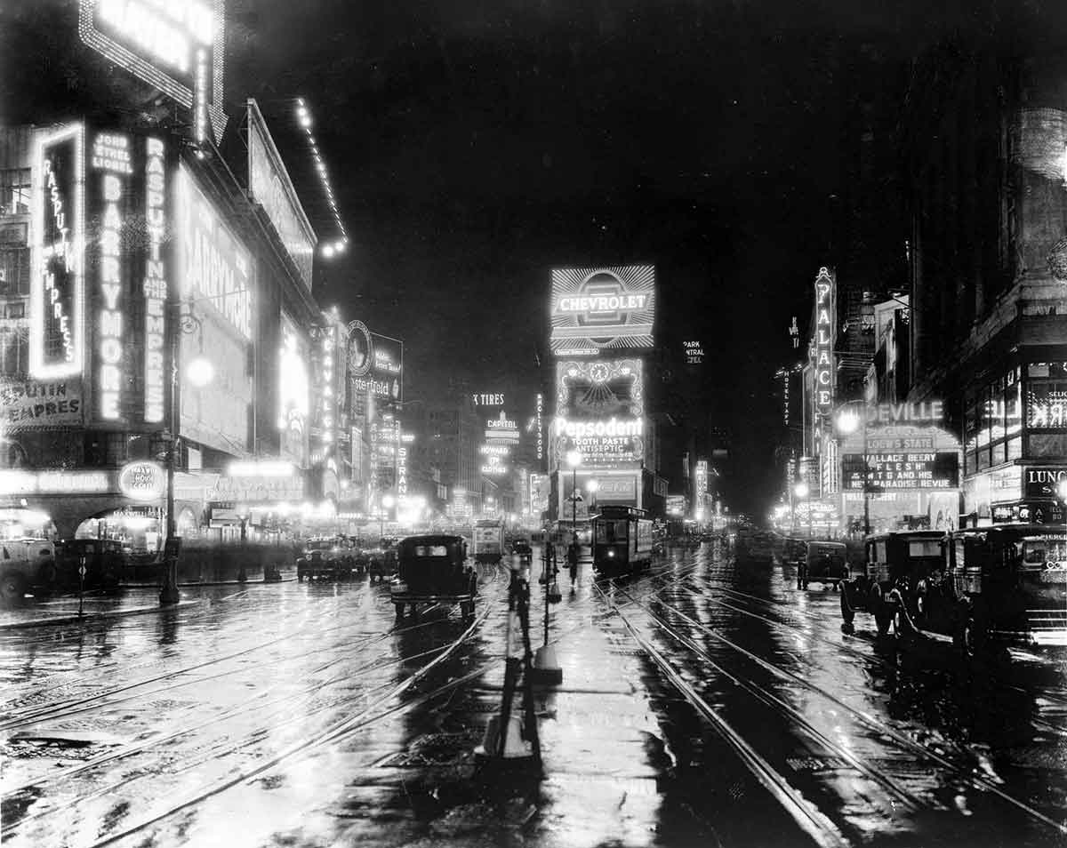 Black and white photo of Times Square lit up at night during the early-to-mid 1900's.