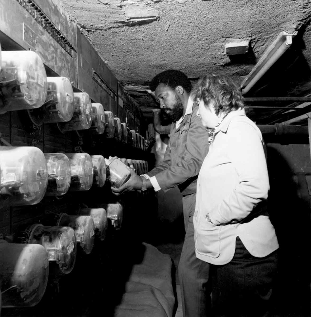 Fotografía en blanco y negro de dos trabajadores de Con Edison mirando una pared con contadores.