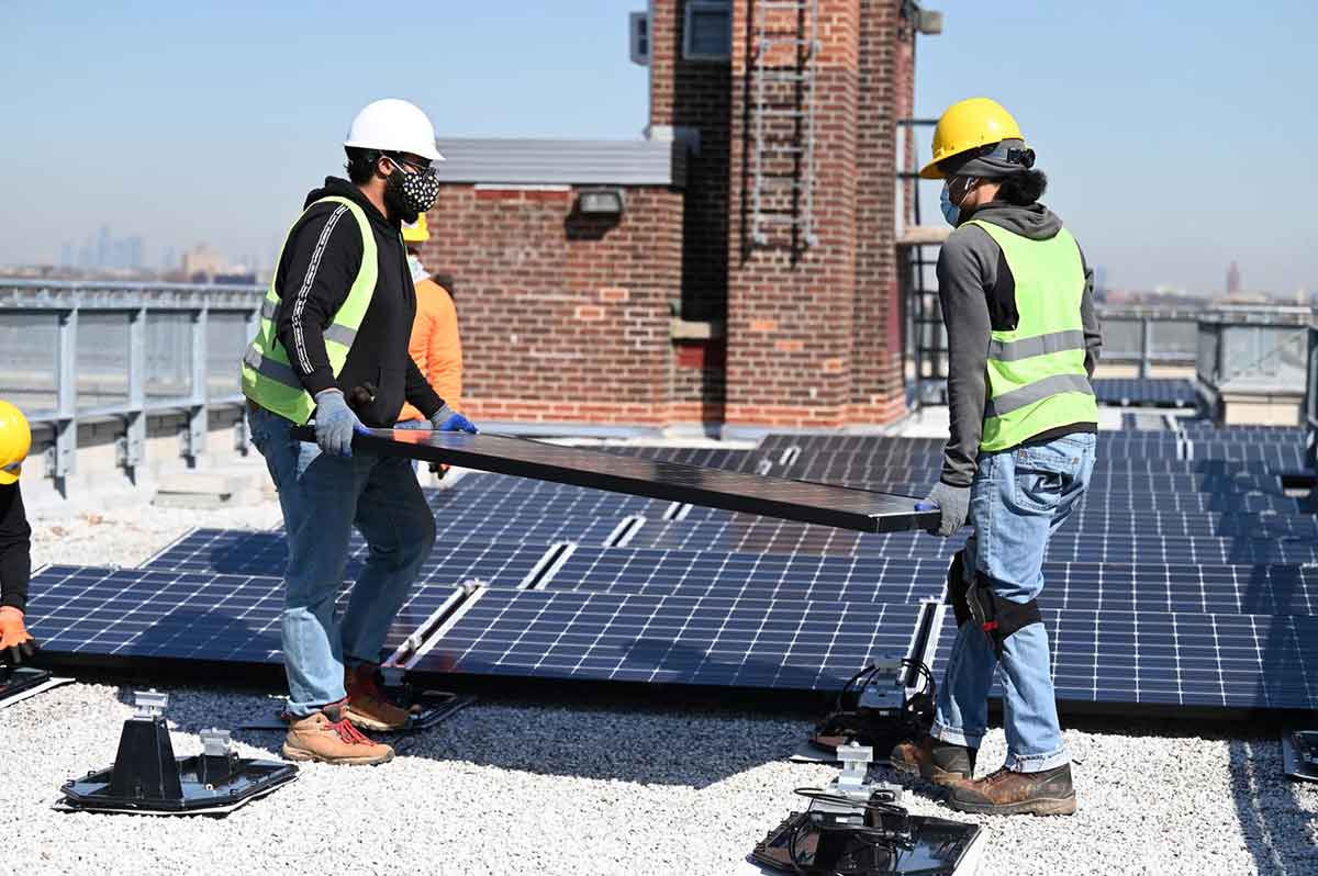 Workers install solar panels on the roof of a building in New York.