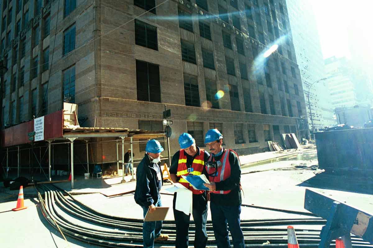 Three Con Edison employees look at plans on a New York City Street.