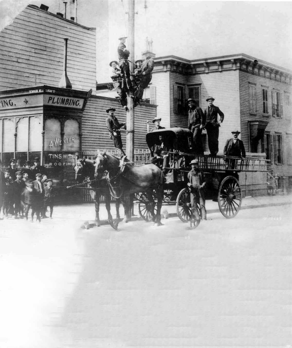Fotografía histórica de trabajadores ascendiendo por un poste para servicios públicos.