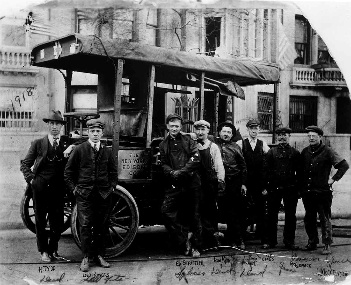 Black and white photo of workers posing for a photo by their work vehicle.