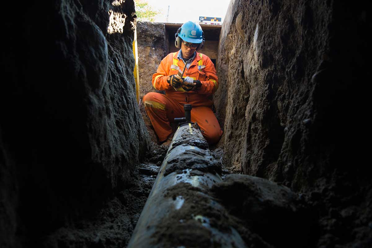 A Con Edison worker installs gas mains along a tunnel dug into a street.