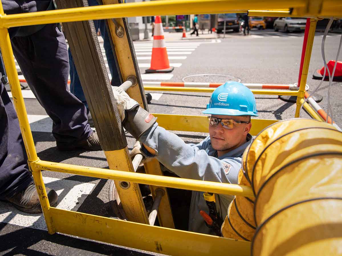 A Con Edison worker climbs out of a manhole. 