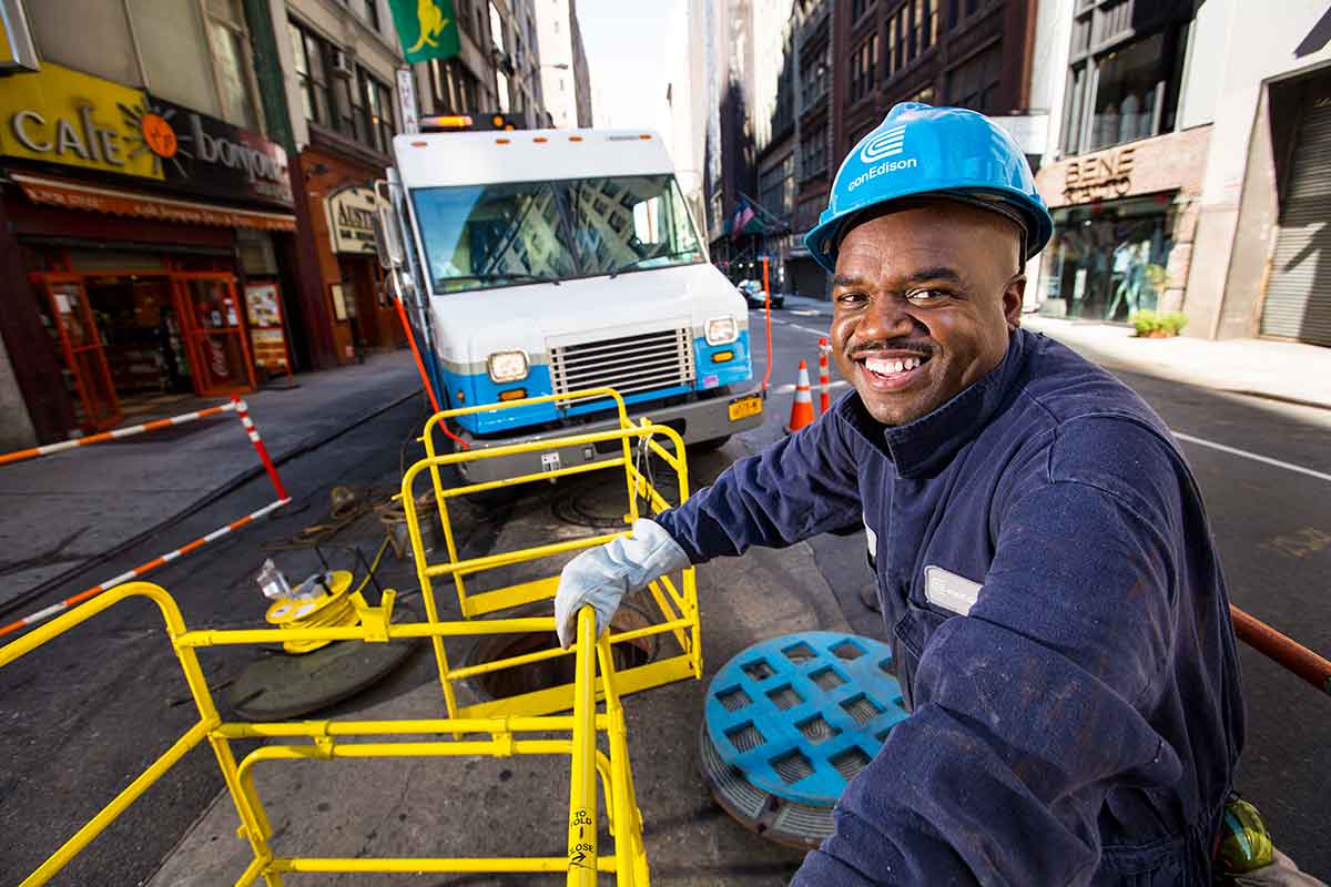 A Con Edison steam worker poses for a photo while halfway down a manhole.