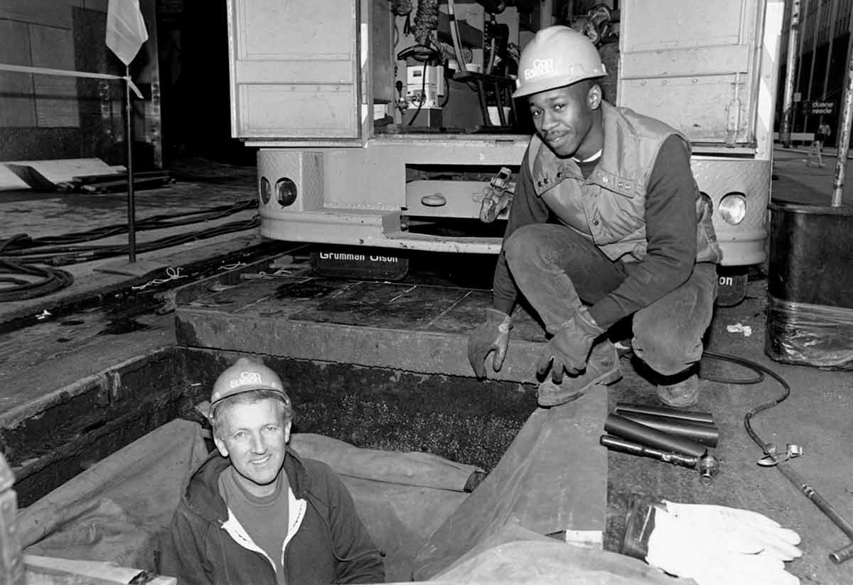 Black and white photo of two Con Edison workers posing by a manhole.