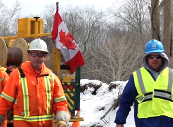 Un trabajador de Canadian Mutual Aid y un trabajador de Con Edison en un sitio nevado con la bandera canadiense de fondo