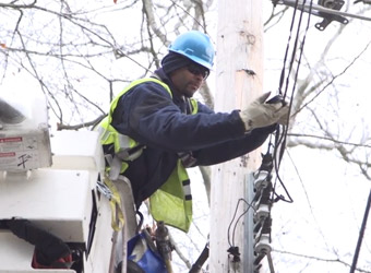 Trabajador de servicios públicos de Con Edison reparando cables en un poste telefónico.