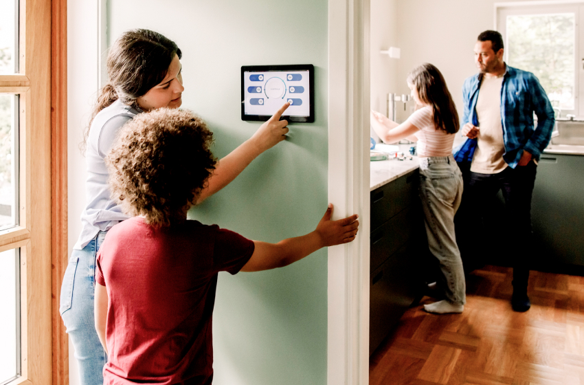 A mother and son set a digital thermostat while a father and daughter clean dishes in the kitchen sink.
