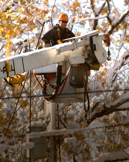 An Orange and Rockland employee in a bucket truck, with tree branches in the background. 