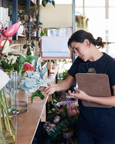 A florist holding flowers and a clipboard while taking on their phone.