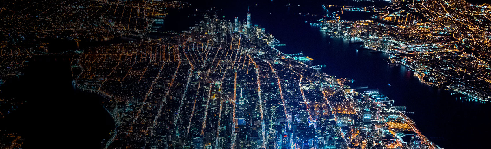 An aerial view of the Manhattan city grid and Jersey shoreline, during the evening. 