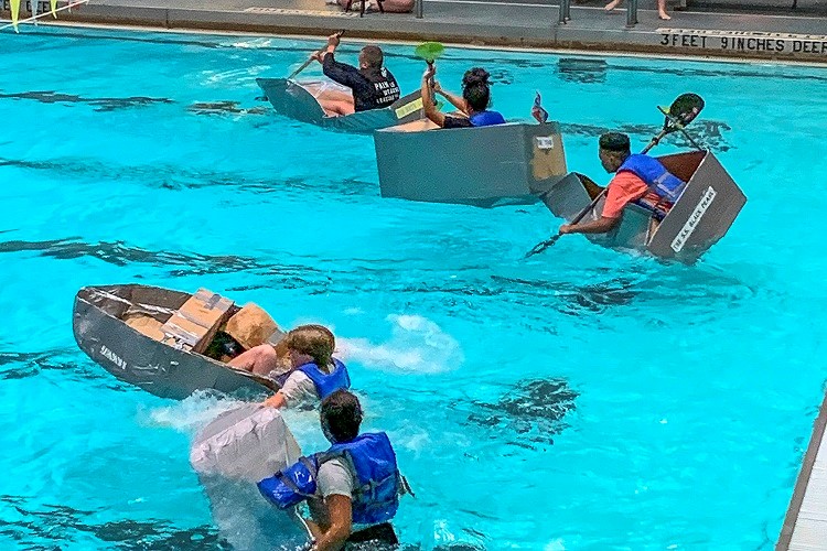 students racing against other home-made cardboard boats in the school’s pool