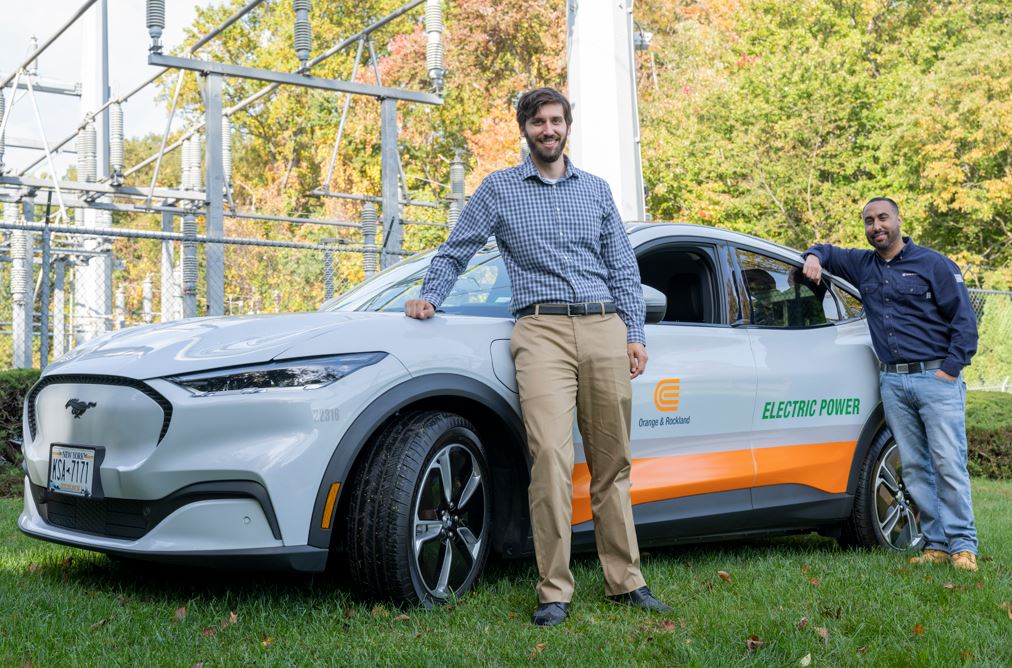Two men standing next to an electric car.