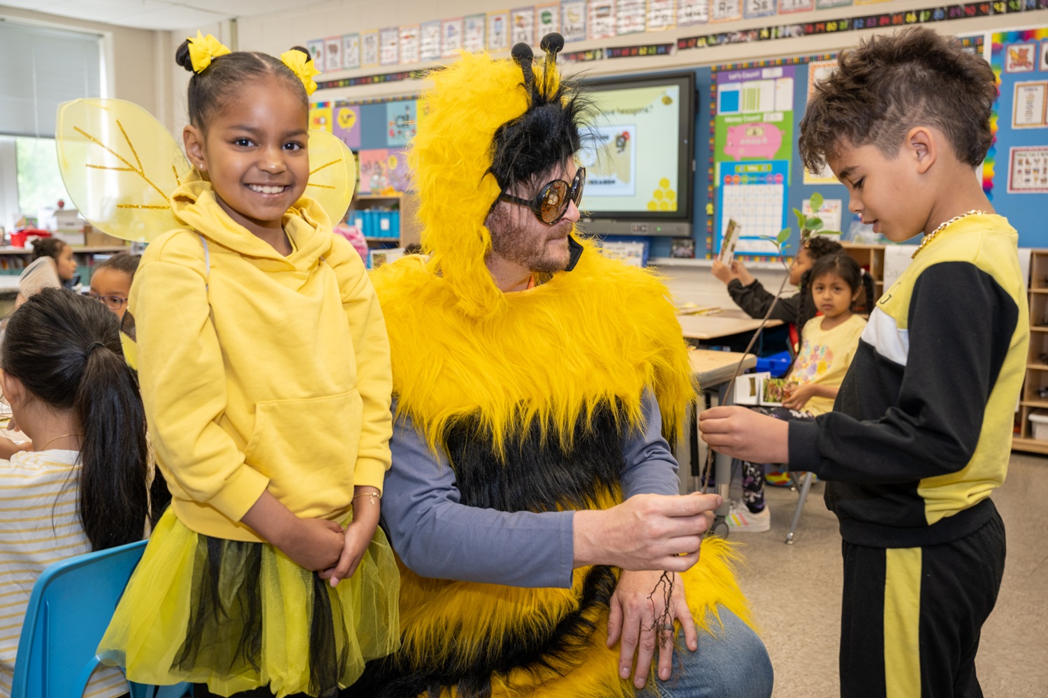 Two students speaking with an educator in a bee costume. 