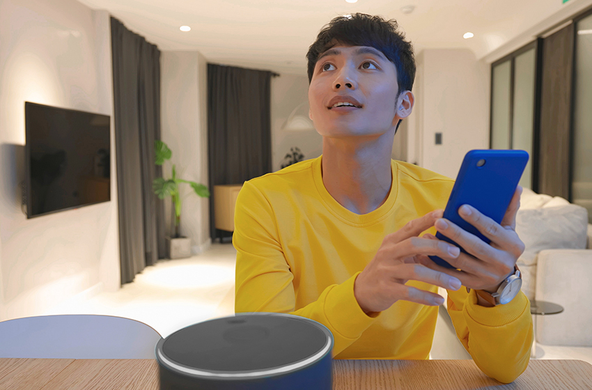 A person wearing a yellow sweater holds a smartphone indoors at a desk.